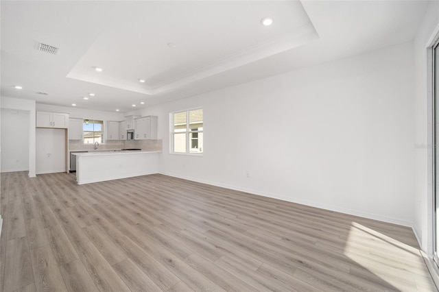 unfurnished living room featuring a raised ceiling and light hardwood / wood-style flooring