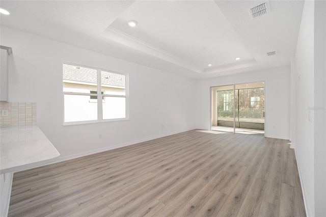 empty room with a tray ceiling and light hardwood / wood-style flooring