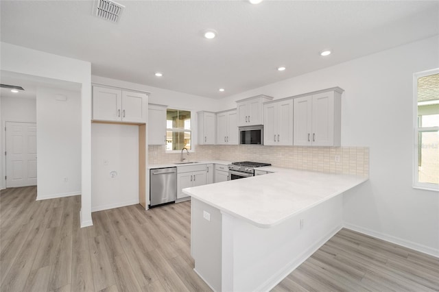 kitchen featuring kitchen peninsula, appliances with stainless steel finishes, sink, light hardwood / wood-style flooring, and white cabinets