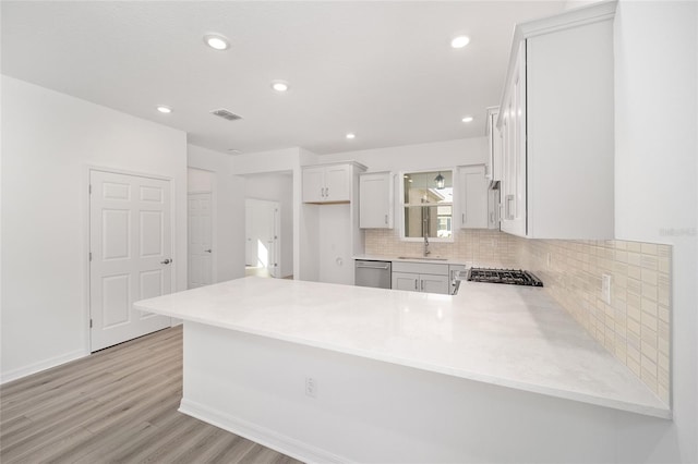 kitchen featuring kitchen peninsula, appliances with stainless steel finishes, light wood-type flooring, decorative backsplash, and sink