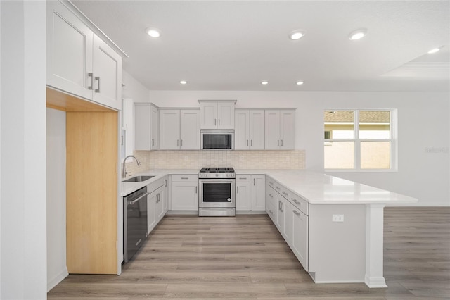 kitchen with white cabinets, sink, light hardwood / wood-style floors, kitchen peninsula, and stainless steel appliances