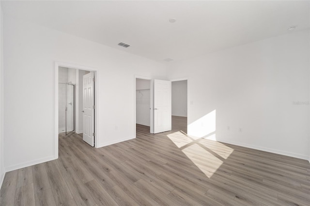 unfurnished bedroom with wood-type flooring, a spacious closet, and a closet