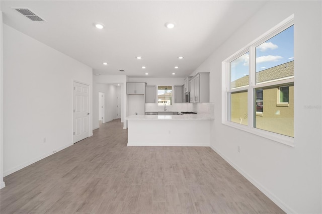 kitchen with kitchen peninsula, light hardwood / wood-style flooring, gray cabinets, and sink