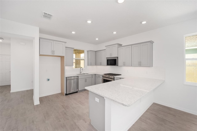 kitchen with gray cabinetry, sink, stainless steel appliances, and light hardwood / wood-style flooring