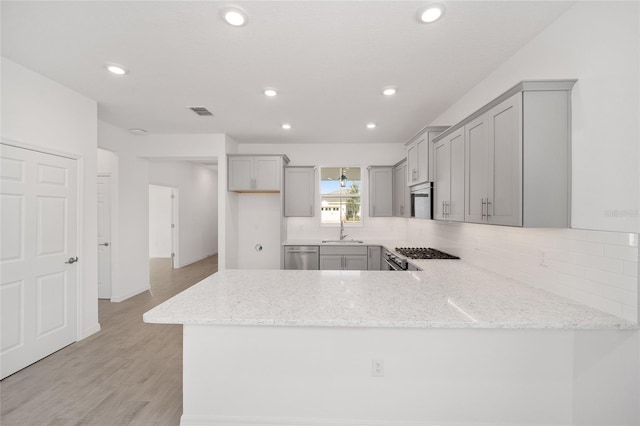 kitchen featuring kitchen peninsula, light stone countertops, sink, gray cabinets, and light hardwood / wood-style floors