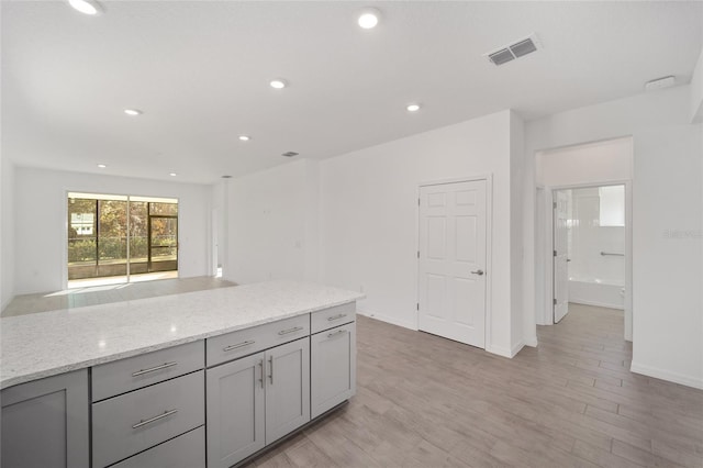 kitchen with gray cabinets, light hardwood / wood-style floors, and light stone countertops