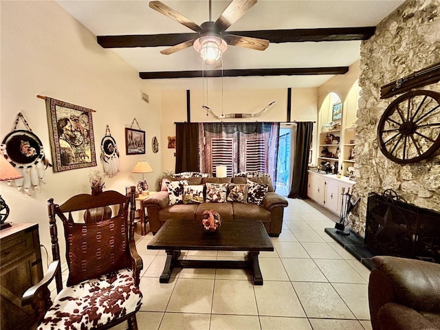 tiled living room featuring beam ceiling, a stone fireplace, and ceiling fan