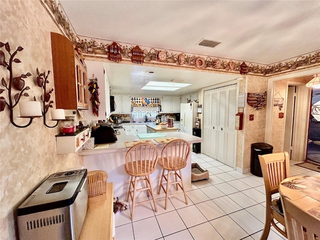 kitchen featuring sink, kitchen peninsula, light tile patterned floors, white cabinetry, and a breakfast bar area