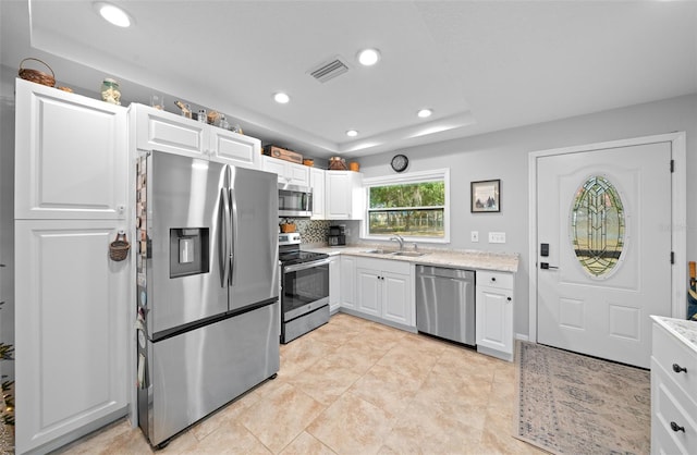 kitchen with sink, light tile patterned floors, tasteful backsplash, white cabinets, and appliances with stainless steel finishes