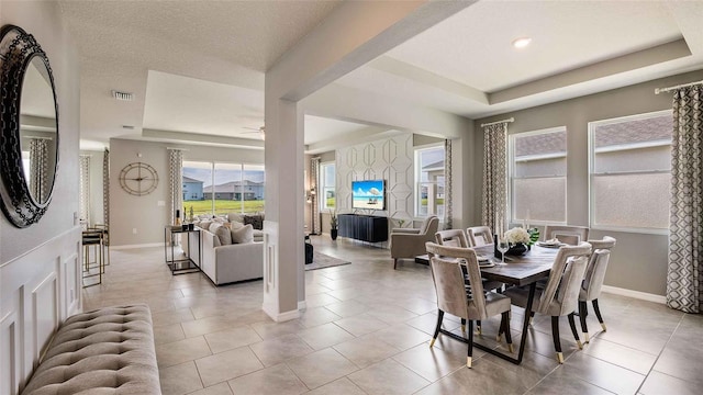 tiled dining space featuring a raised ceiling and ceiling fan