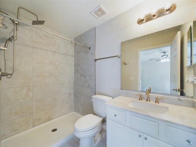 bathroom with ceiling fan, a textured ceiling, tiled shower, toilet, and vanity