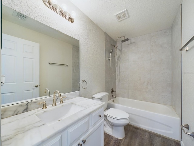 full bathroom with wood-type flooring, a textured ceiling, toilet, vanity, and tiled shower / bath