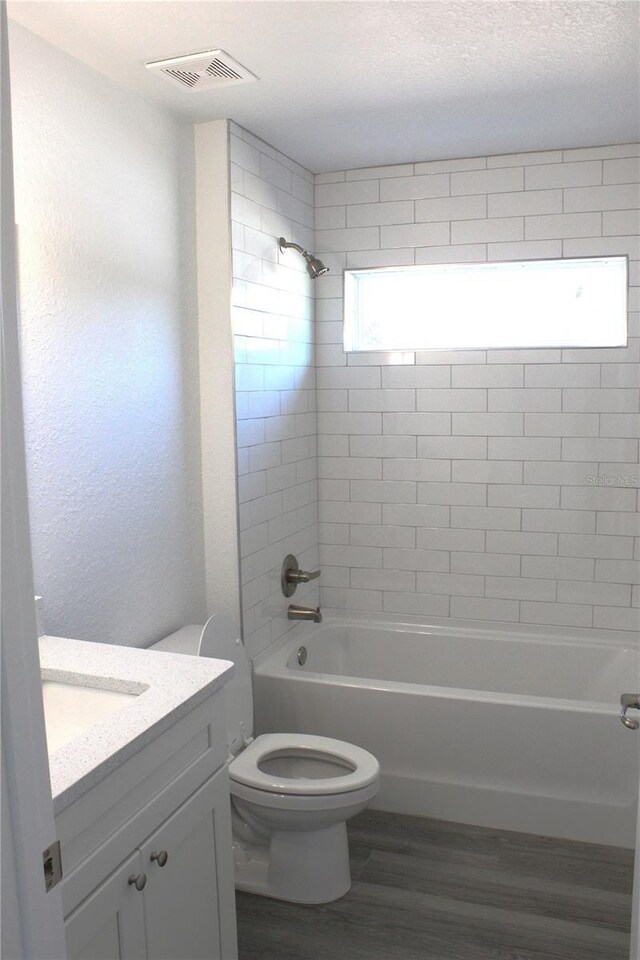 full bathroom with hardwood / wood-style flooring, tiled shower / bath, vanity, and toilet