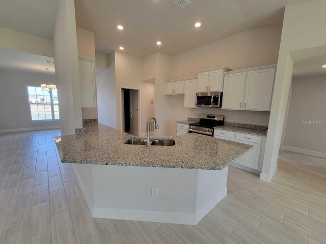 kitchen with white cabinetry, kitchen peninsula, appliances with stainless steel finishes, light stone counters, and sink