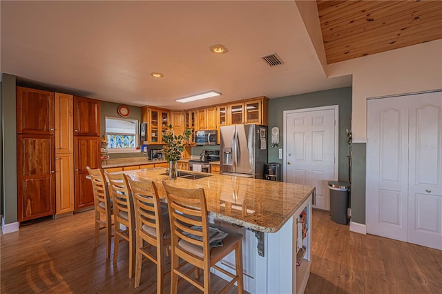 kitchen featuring light stone countertops, stainless steel appliances, a breakfast bar area, a center island with sink, and hardwood / wood-style flooring