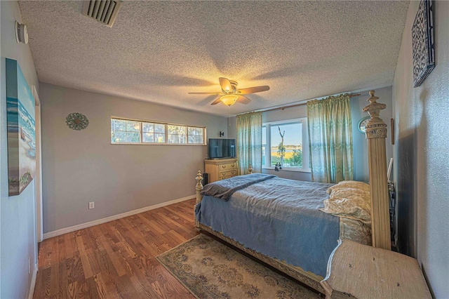 bedroom with a textured ceiling, multiple windows, dark wood-type flooring, and ceiling fan