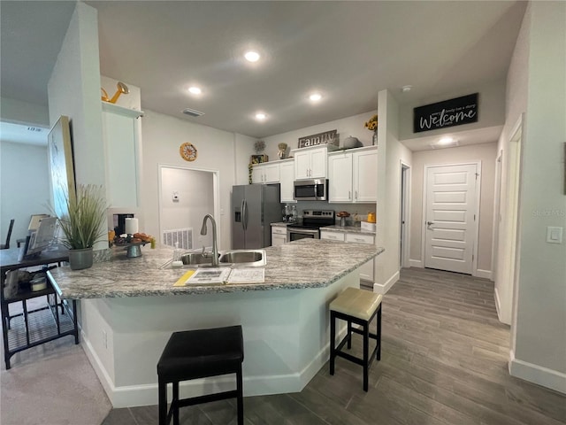 kitchen with kitchen peninsula, a breakfast bar area, appliances with stainless steel finishes, white cabinets, and sink