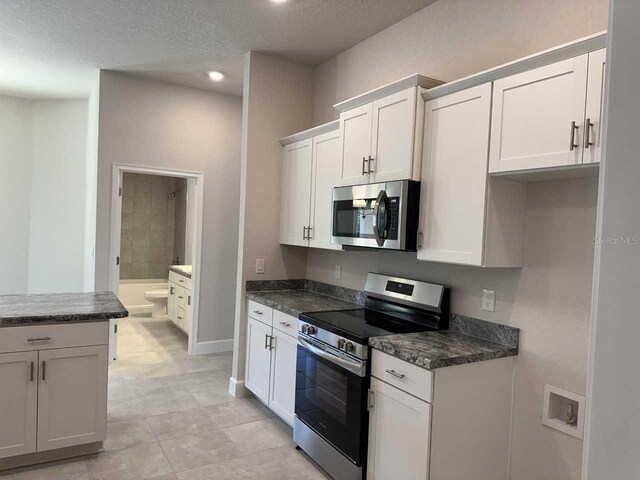 kitchen with a textured ceiling, appliances with stainless steel finishes, and white cabinetry