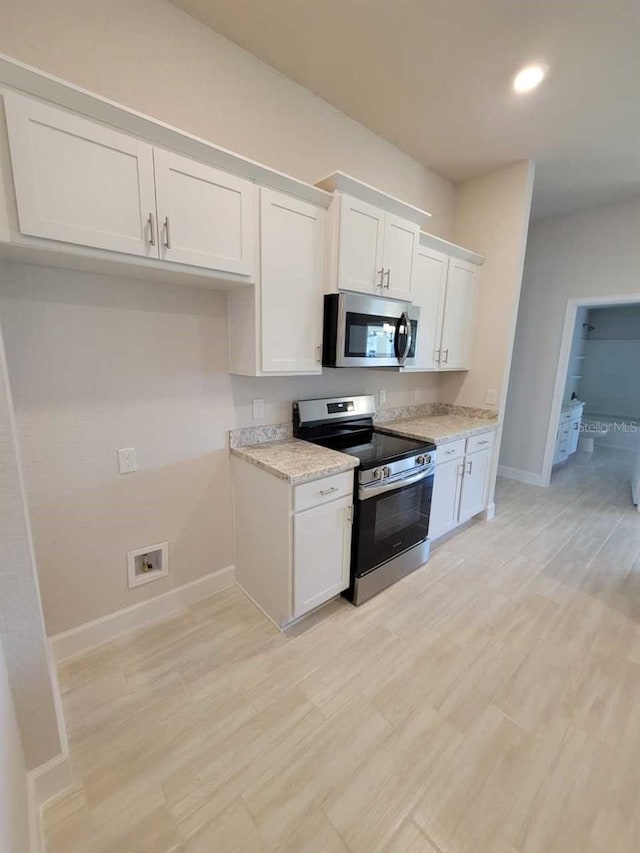 kitchen with light wood-type flooring, appliances with stainless steel finishes, white cabinetry, and light stone counters