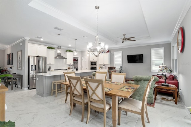 dining space featuring a raised ceiling, sink, ceiling fan with notable chandelier, and ornamental molding