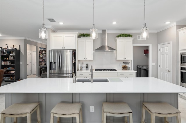 kitchen with sink, wall chimney range hood, separate washer and dryer, a large island with sink, and appliances with stainless steel finishes