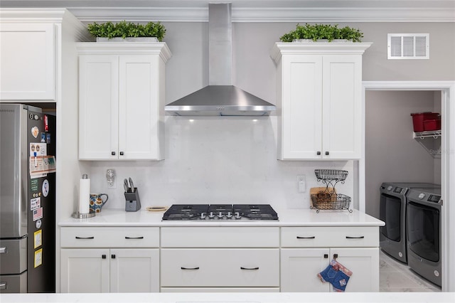 kitchen featuring washing machine and clothes dryer, white cabinetry, wall chimney exhaust hood, appliances with stainless steel finishes, and ornamental molding