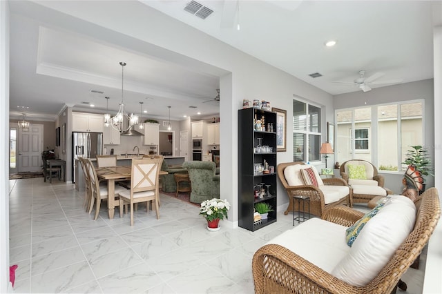 living room featuring ceiling fan with notable chandelier, ornamental molding, and sink