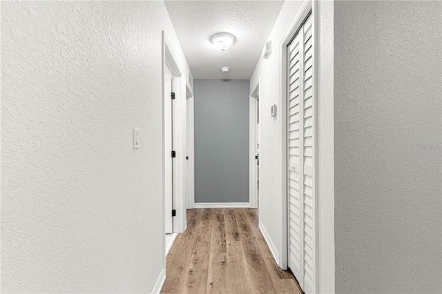 hall with light hardwood / wood-style floors and a textured ceiling