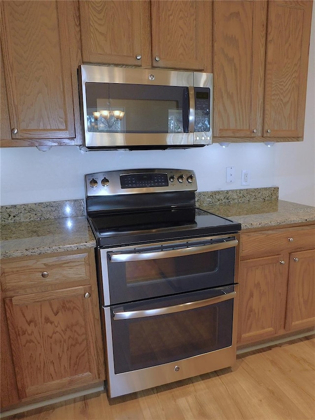 kitchen with a notable chandelier, light stone countertops, appliances with stainless steel finishes, and light hardwood / wood-style flooring