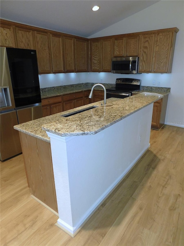 kitchen with light hardwood / wood-style floors, lofted ceiling, a kitchen island with sink, and appliances with stainless steel finishes