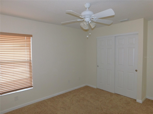 unfurnished bedroom with ceiling fan, multiple windows, light carpet, and a closet