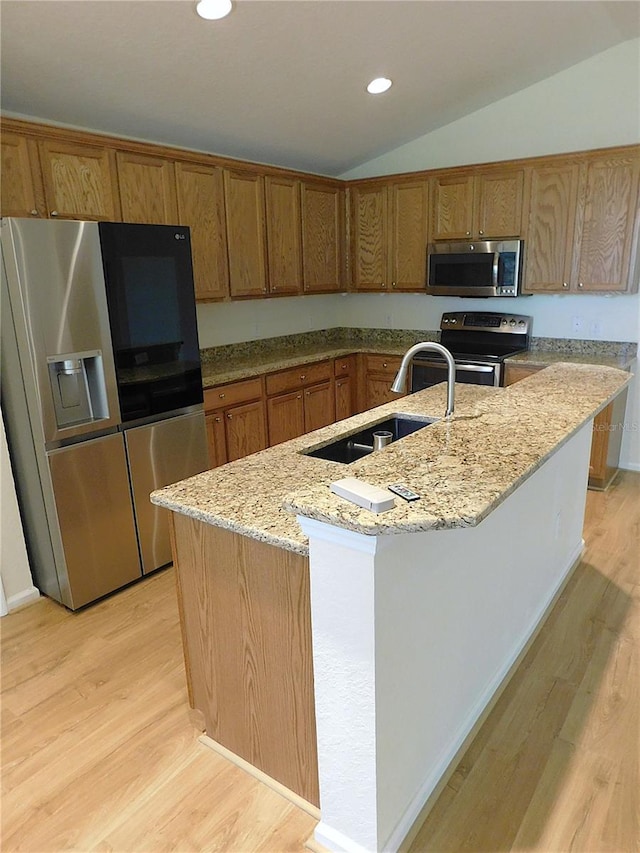kitchen with a sink, light wood-style floors, light stone counters, and appliances with stainless steel finishes