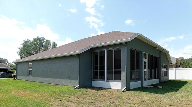 view of side of property featuring a sunroom, stucco siding, fence, and a lawn