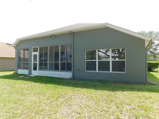 rear view of property with a yard, stucco siding, and a sunroom