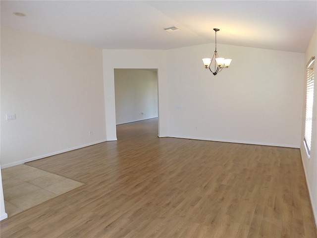 empty room featuring an inviting chandelier, wood finished floors, visible vents, baseboards, and vaulted ceiling