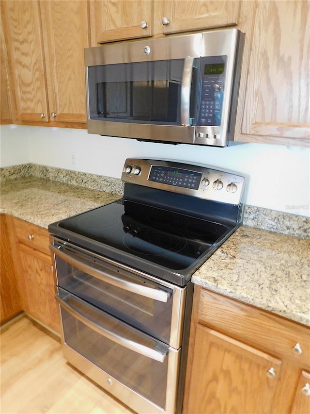 kitchen with light wood-style floors, stainless steel appliances, and light stone countertops