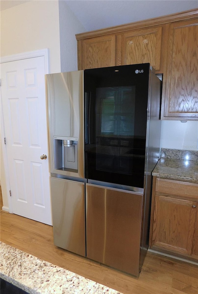 kitchen featuring brown cabinetry, light stone countertops, light wood-type flooring, and stainless steel refrigerator with ice dispenser