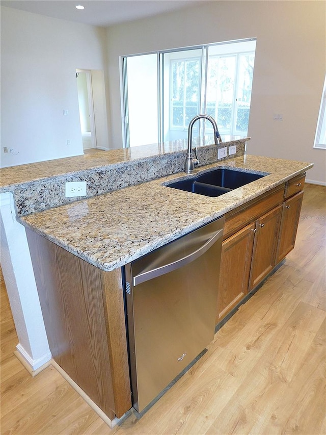 kitchen featuring a sink, brown cabinets, a kitchen island with sink, dishwasher, and light wood-style floors