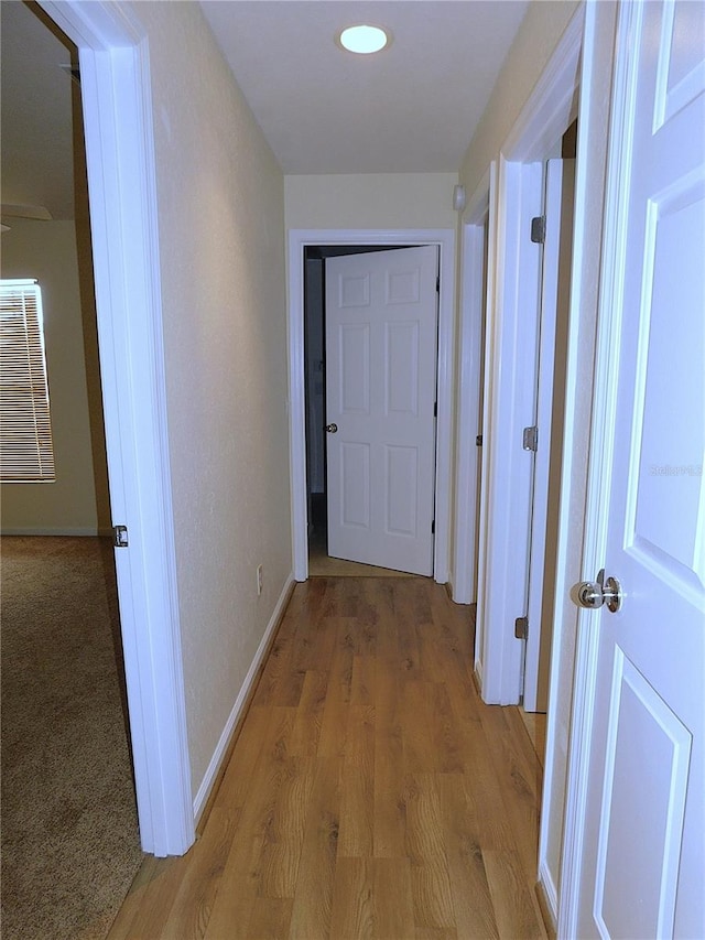 hall featuring baseboards, light wood finished floors, and recessed lighting