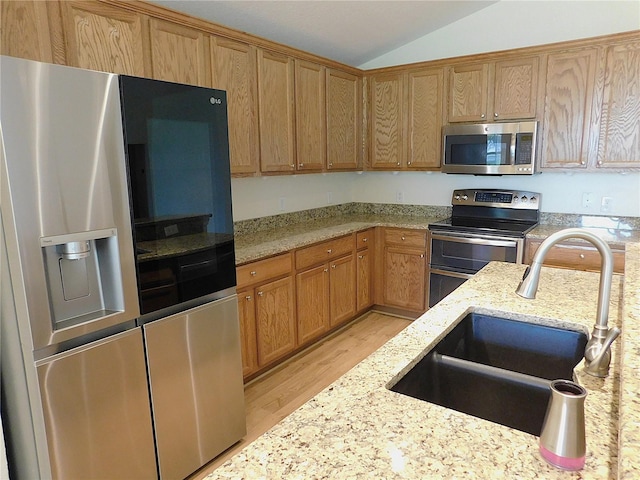 kitchen featuring a sink, lofted ceiling, stainless steel appliances, light stone counters, and light wood-style floors