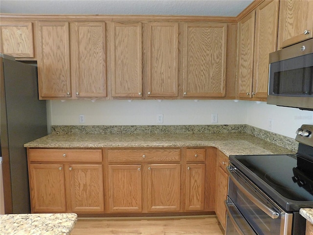 kitchen with light stone counters, light wood finished floors, and appliances with stainless steel finishes