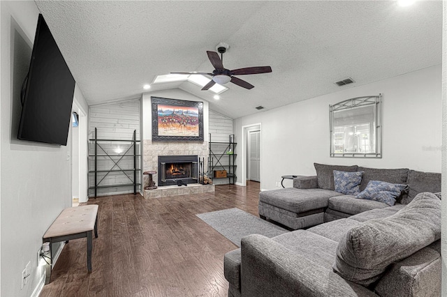 living room with a textured ceiling, a stone fireplace, vaulted ceiling, and hardwood / wood-style flooring