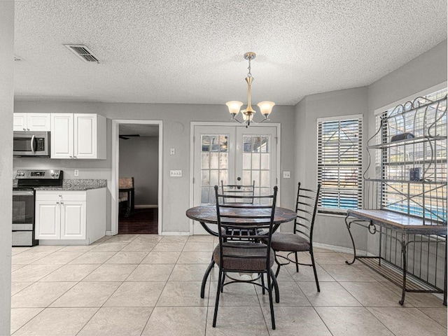 tiled dining room featuring french doors, a textured ceiling, and a chandelier