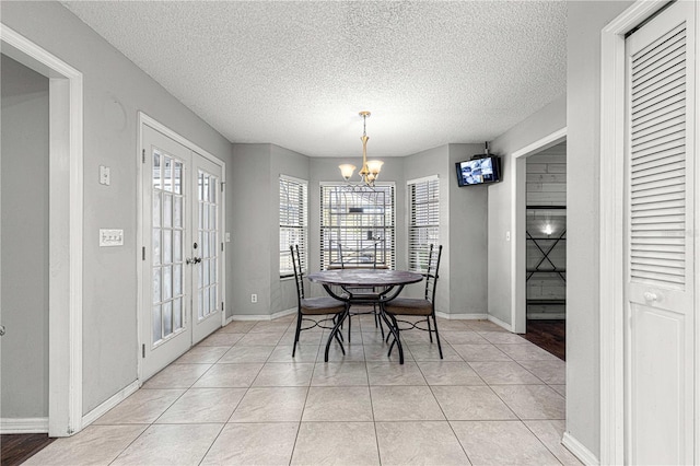 tiled dining space with an inviting chandelier, a textured ceiling, and french doors