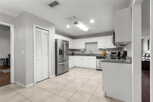 kitchen with white cabinets, sink, light tile patterned floors, a textured ceiling, and appliances with stainless steel finishes