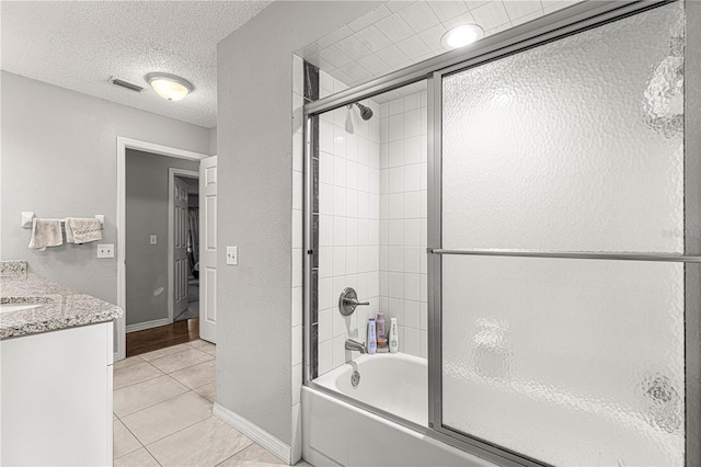 bathroom with tile patterned flooring, a textured ceiling, vanity, and combined bath / shower with glass door