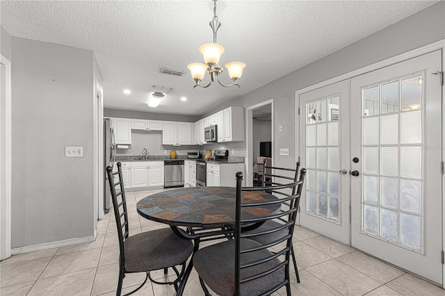 tiled dining area with sink, french doors, a textured ceiling, and an inviting chandelier