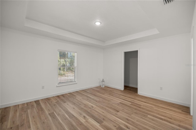 spare room with a tray ceiling and light hardwood / wood-style flooring