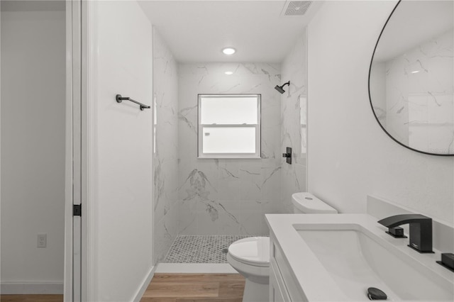 bathroom with a tile shower, vanity, wood-type flooring, and toilet