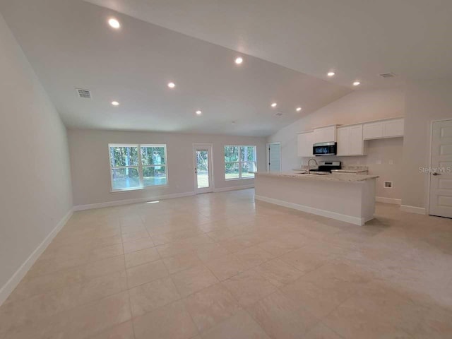 kitchen with light stone countertops, appliances with stainless steel finishes, white cabinetry, vaulted ceiling, and a center island with sink